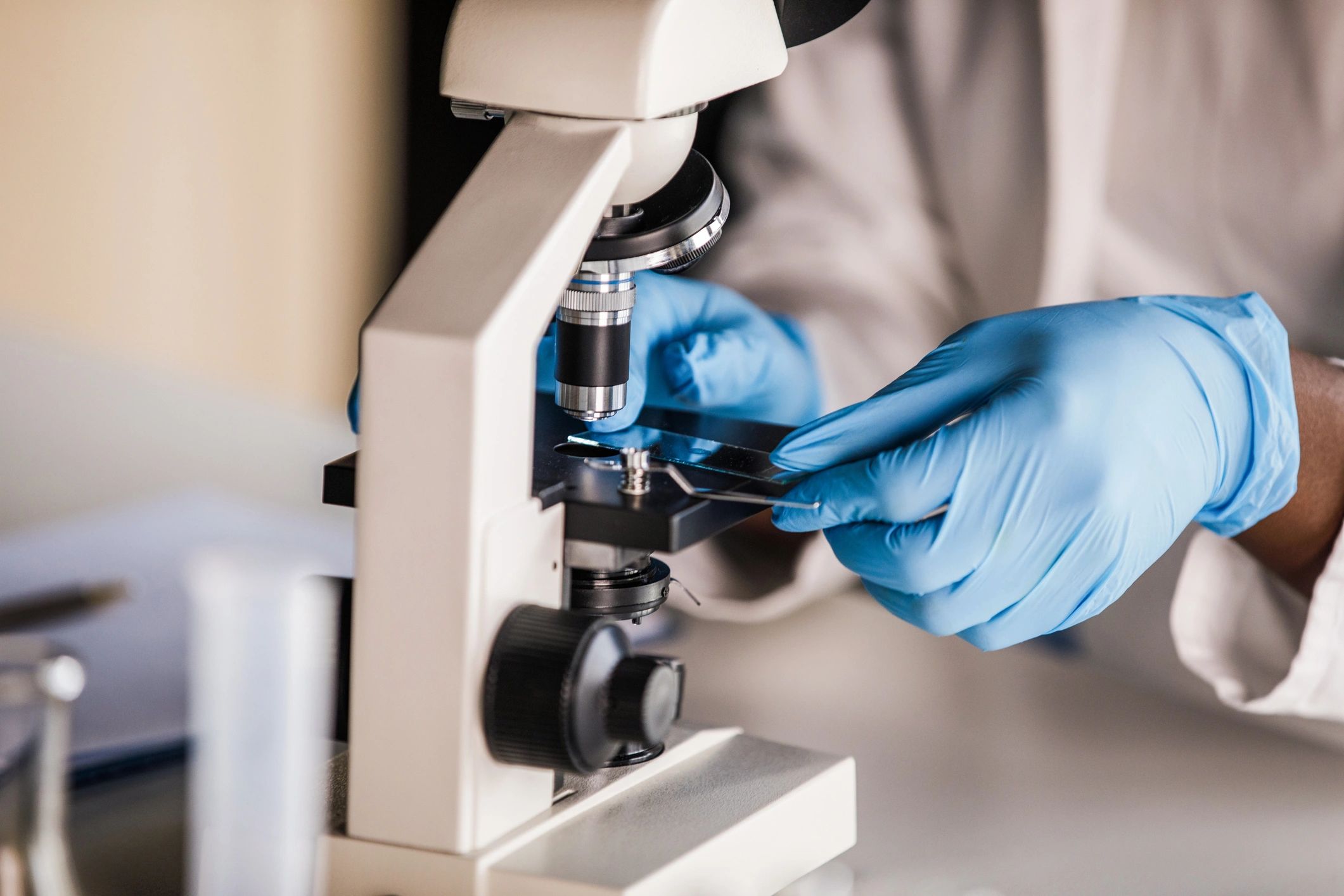 Lab technician in protective gloves placing a sample slide under a microscope
